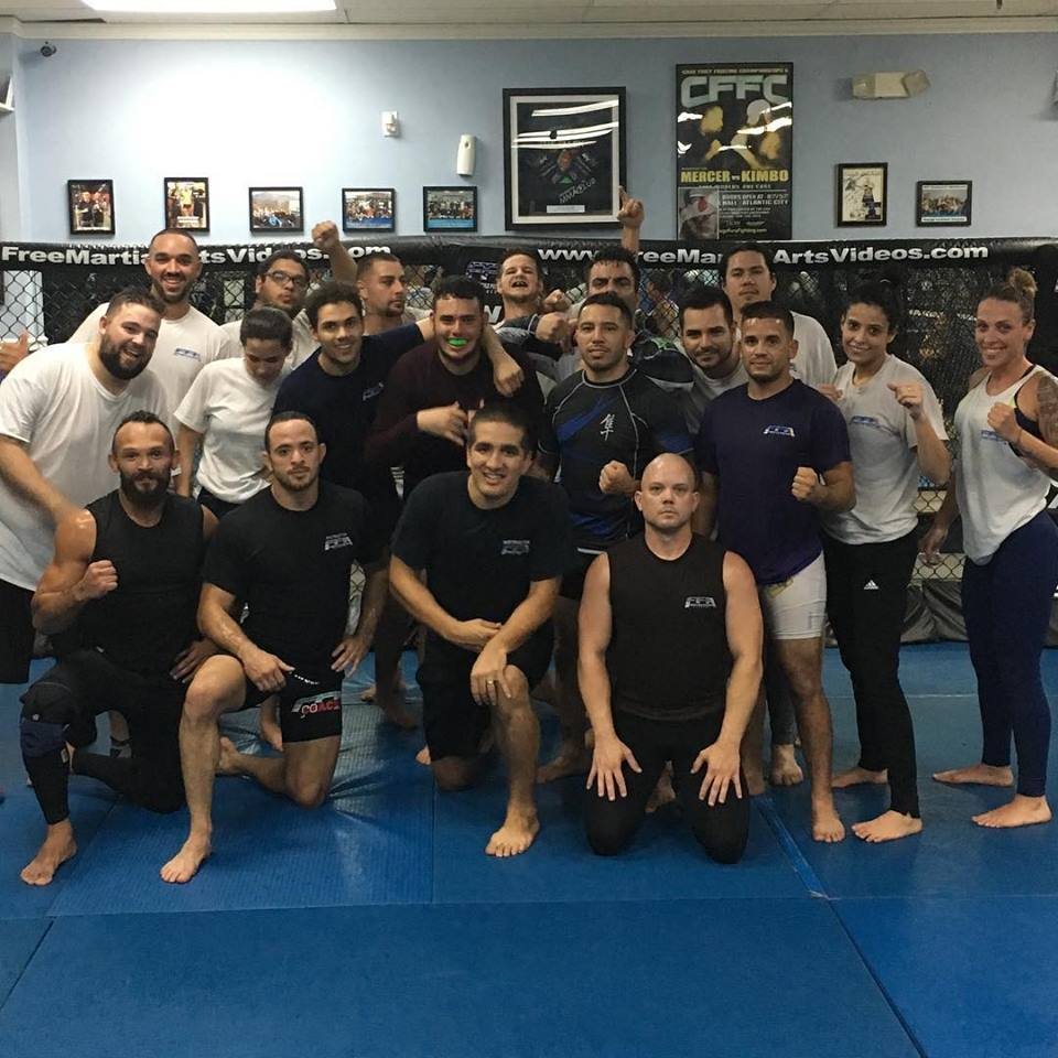 A group of adult students posing on the mats in front of the cage